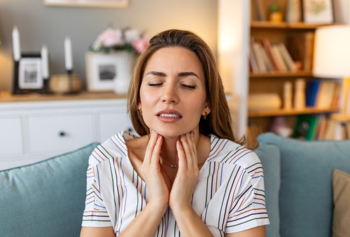 Close up of young woman rubbing her inflamed tonsils, tonsilitis problem, cropped. Woman with thyroid gland problem, touching her neck, girl has a sore throat